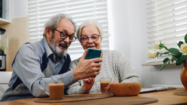 An older couple looking at a cell phone while sitting at a dining room table